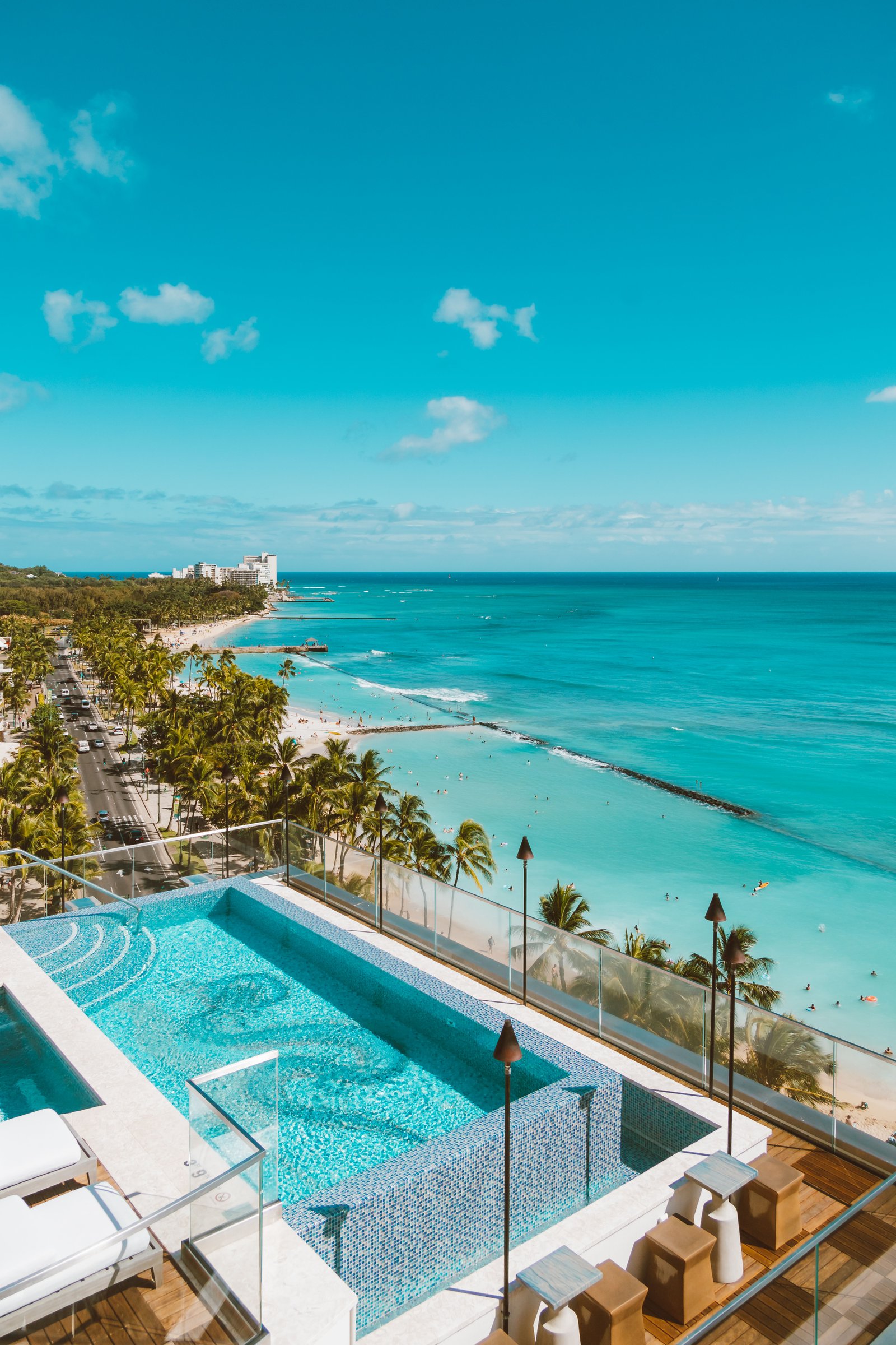 Luxury wellness travel resort pool overlooking a tropical coastline with a laptop on an outdoor desk.