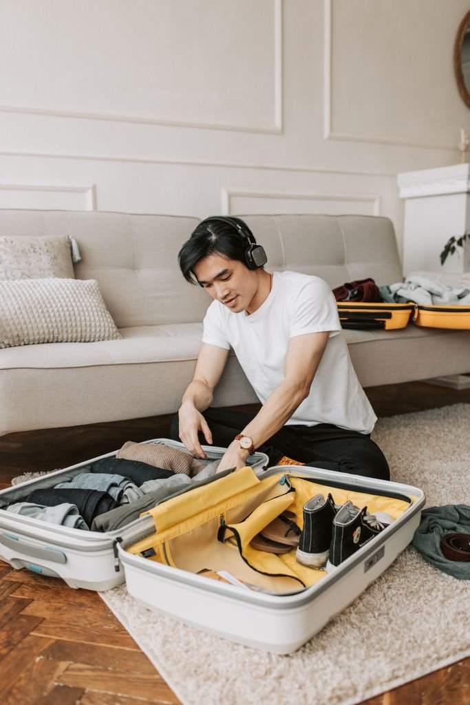 Young man packing suitcase in living room while listening to music.