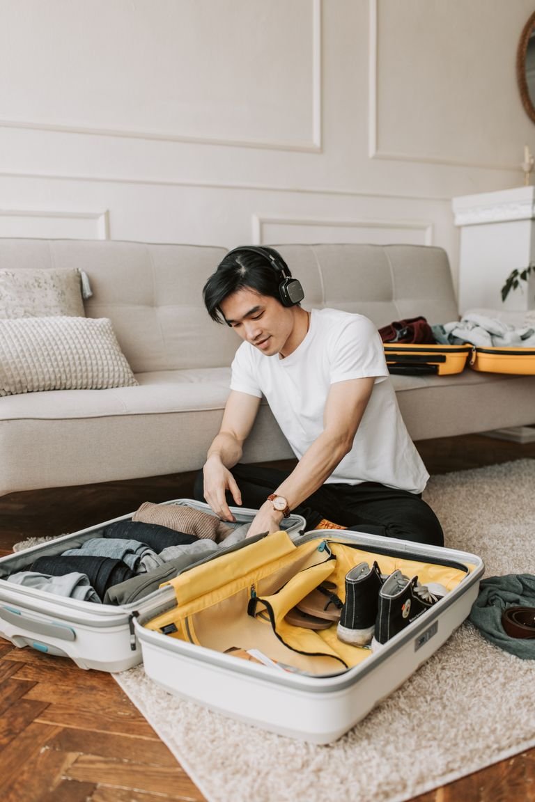 Young man packing suitcase in living room while listening to music.